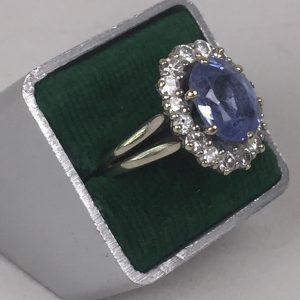 Bague marguerite en or gris 18K ou platine centrée d'une pierre bleue facetée montée en serti-griffes, dans un entourage de seize petits diamants.(...)