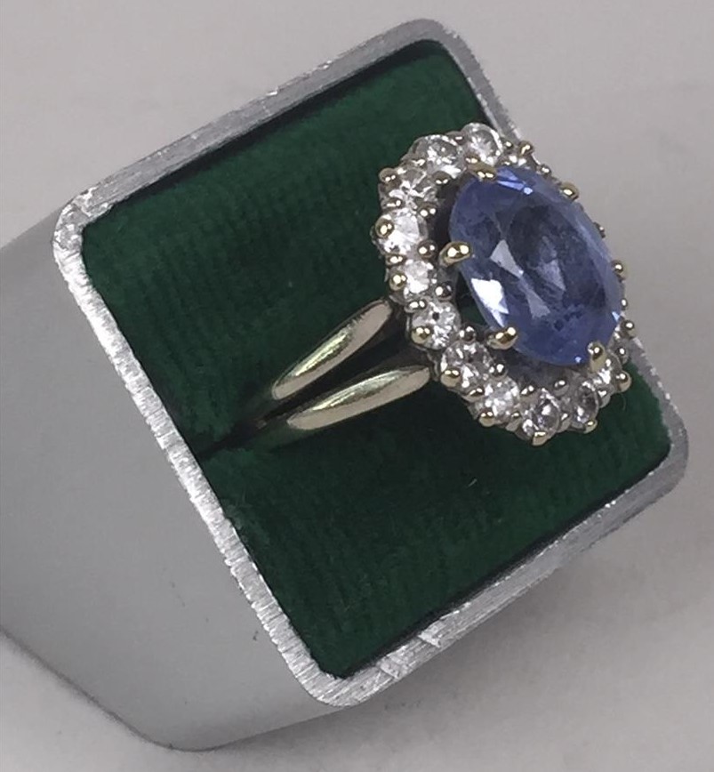 Bague marguerite en or gris 18K ou platine centrée d'une pierre bleue facetée montée en serti-griffes, dans un entourage de seize petits diamants.(...)